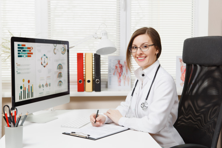 A nurse working on a computer and smiling. 