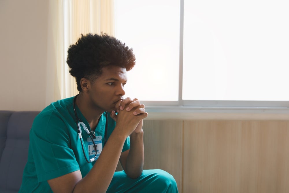 A nurse sits in a room with a discouraged expression. 