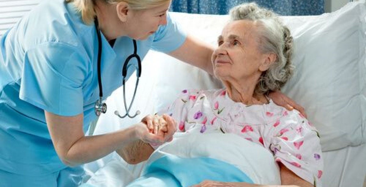 Nurse tending to elderly patient in hospital bed