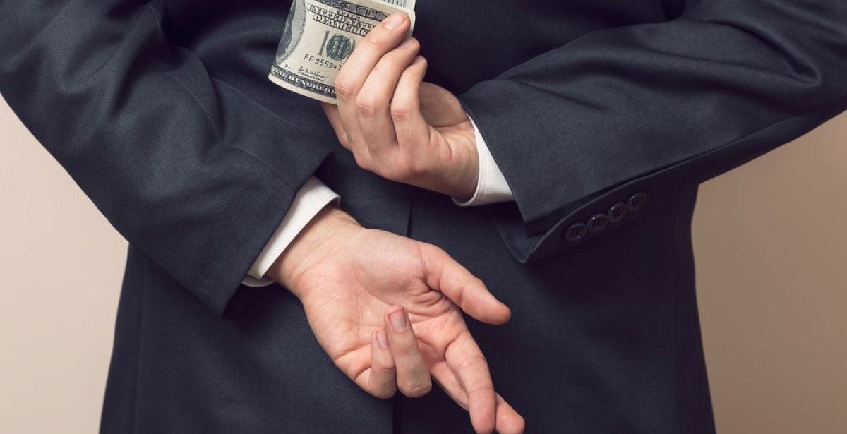 Businessman in a suit holding his hands behind his back with stack of dollar banknotes in one and fingers crossed on another one