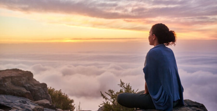 Woman on mountaintop looking out over clouds at sunrise