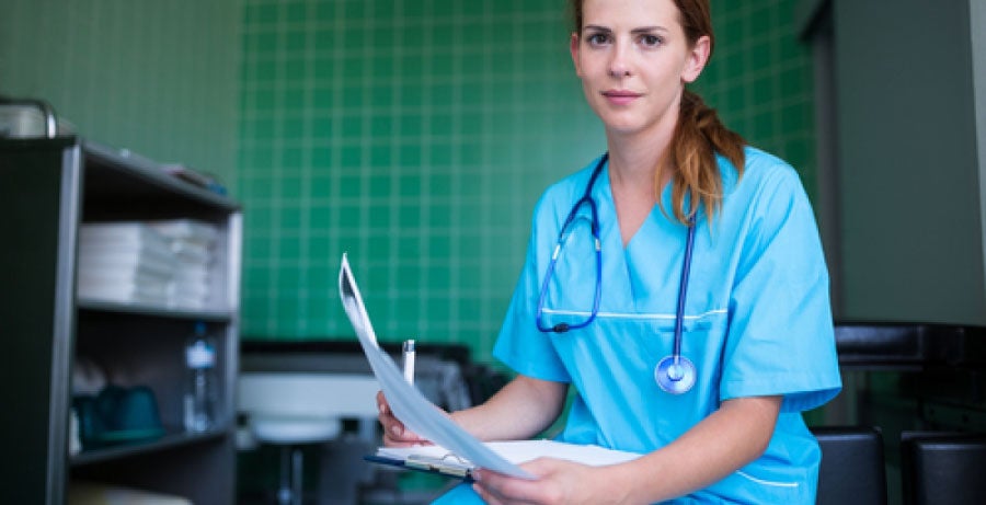 Nurse practitioner wearing scrubs and holding medical chart in hospital room